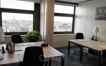 Heldere kantoorruimte te huur in Antwerpen Centrum met uitzicht op de stad. Twee werkplekken, planten en kantooraccessoires bij het raam met stadszicht op De Keyserlei 58-60.