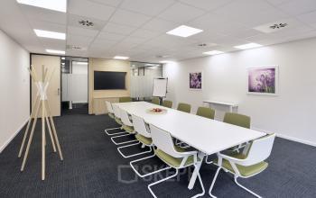 Vergaderruimte met witte tafel, groene stoelen, flip-over en een scherm aan de muur in een kantoor te huur op Noorderlaan 147, Antwerpen Merksem.
