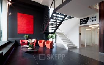 Moderne kantoorruimte te huur in Antwerpen Wommelgem, Nijverheidsstraat 70, met stijlvolle zitruimte, zwarte vloertegels, en een opvallende rode muurdecoratie.