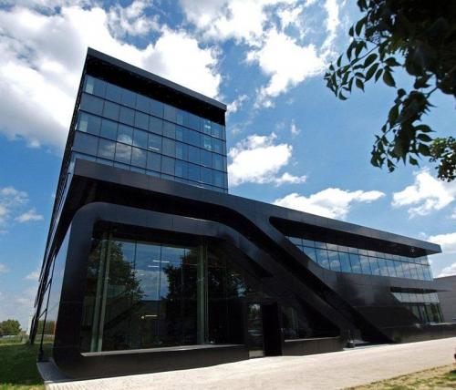 Modern zwart kantoorgebouw gelegen op Nijverheidsstraat 70, Antwerpen Wommelgem, Antwerpen. Het gebouw heeft een opvallende glazen gevel en een uniek ontwerp met schuine lijnen. Kantoorruimte te huur beschikbaar.