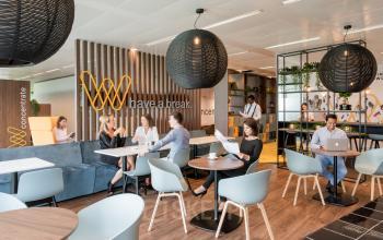 Gezellige kantoorruimte te huur op Leonardo Da Vincilaan 1, Brussel Airport. Moderne inrichting met zithoek, tafels en stoelen. Mensen zijn aan het werken en overleggen.