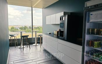 Gemeubileerde pantry van kantoor te huur in Brussel Airport op Leonardo Da Vincilaan 19, met koffiezetapparaat en zitgedeelte, naast een raam met uitzicht.