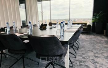 Stijlvolle vergaderruimte met grote tafel en comfortabele stoelen in kantoor te huur op Leonardo Da Vincilaan 19, Brussel Airport, Brussel. Waterflessen en notitieblokken op tafel.