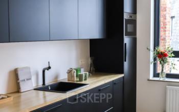Moderne keuken in een kantoorruimte te huur op Rue du Congres 37, Brussel. Zwart meubilair, houten werkblad, magnetron en spoelbak aanwezig.