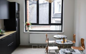 Vergaderruimte met moderne keuken aan Rue du Congres 37, Brussel. Mooie werkplek met zwarte kasten, ramen die veel licht binnenlaten en tafels met stoelen.