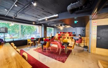 Koffiehoek en ontspanningsruimte in kantoor te huur op Louizalaan / Avenue Louise 523, Brussel Elsene. Mensen zitten aan tafels in gesprek, ingericht met kleurrijke stoelen en banken.