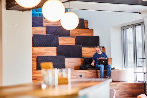 Man met laptop in informele vergaderruimte met houten zitplaatsen, kantoorpand Louizalaan / Avenue Louise 54, Brussel Elsene.