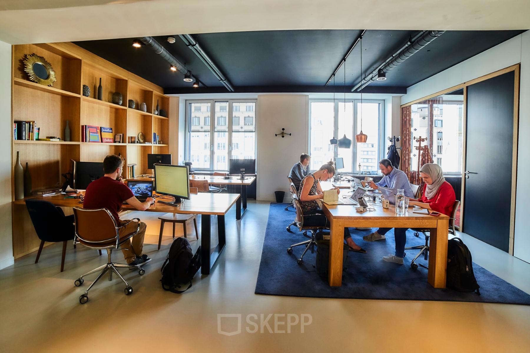 Kantoor te huur aan de Louizalaan 54 in Brussel Elsene, moderne kantoorruimte met grote ramen en houten meubels, mensen aan het werk achter computers.