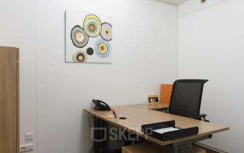 Kantoorruimte te huur met een bureau, stoel en kleurrijk kunstwerk aan de muur. De ruimte bevindt zich op Schumanplein / Rond-Point Robert Schuman 6 in Brussel Etterbeek.