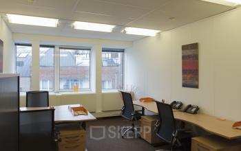 Verlichte kantoorruimte te huur op Schumanplein in Brussel Etterbeek, met moderne bureaus, stoelen en uitzicht op de stad. Ideaal voor een professionele werkomgeving.