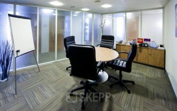 Kantoorruimte te huur in Brussel Etterbeek met moderne voorzieningen, inclusief ronde tafel en stoelen, een flip-over en opbergruimte met telefoons op Schumanplein.