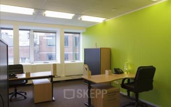Kantoorruimte te huur in Brussel Etterbeek met grote ramen, groene muren en moderne bureaus. Op Schumanplein is deze lichte werkplek ideaal voor zakelijk gebruik.