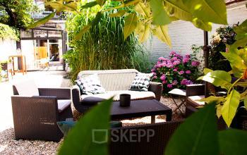 Gezellige gemeubileerde buitenruimte bij het kantoor te huur aan Priester Cuypersstraat / Rue Abbé Cuypers 3 in Brussel Etterbeek, ingericht met comfortabele zitmeubelen omringd door groen en bloemen.