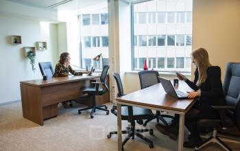 Kantoor te huur op Robert Schumanplein 2-4, Brussel Europese Wijk met lichte werkplekken en bureaus, waar twee personen zakelijke activiteiten uitvoeren.