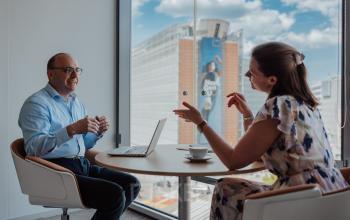 Twee personen voeren een zakelijke bespreking aan een ronde tafel in een modern kantoor te huur met uitzicht op Brussel Europese Wijk.