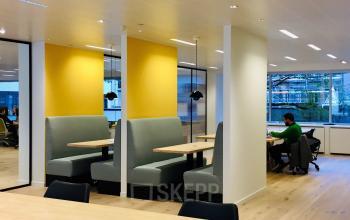 Moderne kantoorruimte te huur op Meeûssquare 35 in Brussel Europese Wijk, met gele en witte muren, comfortabele zitbanken en tafels, waar een persoon aan het werk is met een laptop aan een tafel.