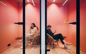 Twee personen in telefooncabines in een kantoorruimte te huur op Meeûssquare / Square de Meeûs 35, Brussel Europese Wijk, Brussel. De ruimte is voorzien van zittend meubilair en heeft een moderne inrichting.