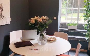 Moderne vergaderruimte met ronde tafel, vier stoelen, een laptop en bloemen, in kantoor te huur op Breydelstraat / Rue Breydel 34-36, Brussel Europese Wijk.