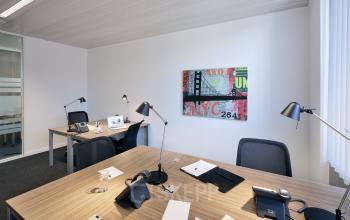 Moderne gemeubileerde kantoorruimte te huur met vier werkplekken en kleurrijk schilderij aan de muur, gelegen op Place Marcel Broodthaers 8 in Brussel-Zuid.