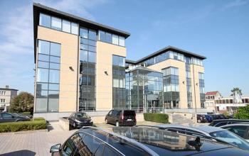 Exterieur van kantoorgebouw op Pontbeekstraat 2-4, Dilbeek. Verschillende auto's geparkeerd voor het moderne pand, dat grote ramen en meerdere verdiepingen heeft. Kantoorruimte te huur beschikbaar.