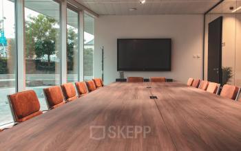 Vergaderzaal met lange tafel, oranje stoelen, groot scherm aan de muur, te huur als kantoorruimte op Oktrooiplein 1, Gent, Gent.