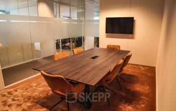 Vergaderzaal met houten tafel, zes bruine stoelen, en een muurtelevisie in een kantoor te huur op Oktrooiplein 1, in Gent.