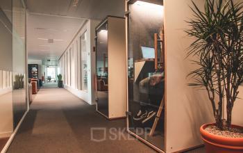 Kantoor te huur op Oktrooiplein 1 in Gent, met moderne glazen wanden, enkele werknemers bezig in afgescheiden werkruimtes.