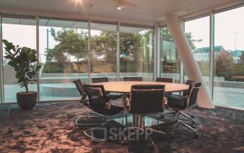 Vergaderruimte met moderne fauteuils en ronde tafel, grote ramen met uitzicht op buitenruimte bij kantoor te huur op Oktrooiplein 1, Gent.