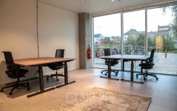 Kantoorruimte te huur bij Oktrooiplein 1 in Gent met ruime werktafels en stoelen, grote ramen voor natuurlijk licht en uitzicht op fietsenstalling.