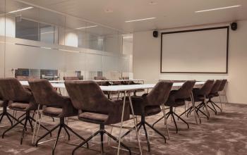 Vergaderzaal te huur in Gent op Oktrooiplein 1, met moderne stoelen en een groot projectiescherm voor zakelijke bijeenkomsten. Ruime en professionele omgeving perfect voor elke vergadering.