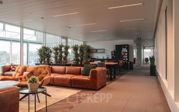 Moderne kantoorruimte te huur op Oktrooiplein 1, Gent, met leren banken, planten en verschillende werkplekken. Enkele mensen zijn hun werkzaamheden aan het verrichten aan hoge tafels bij een aangename, lichte sfeer.