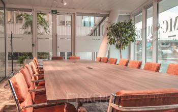 Vergaderruimte in het kantoor te huur op Oktrooiplein 1, Gent. Grote tafel met oranje stoelen, omgeven door ramen en veel groen.