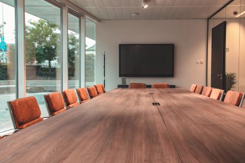 Vergaderzaal met lange tafel, oranje stoelen, groot scherm aan de muur, te huur als kantoorruimte op Oktrooiplein 1, Gent, Gent.