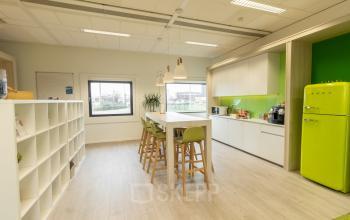 Kantoorruimte te huur aan Atealaan 34A in Herentals met moderne pantry, witte kasten, houten vloer, hoge tafel met groene krukken en een groene vintage koelkast.