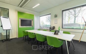Kantoorruimte te huur op Atealaan 34A in Herentals. Moderne vergaderruimte met groene stoelen, witte tafel en grote ramen met uitzicht op bomen.