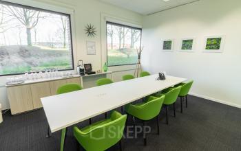 Kantoorruimte te huur op Atealaan 34A, Herentals, met een lange witte tafel, groene stoelen, en drie kunstwerken aan de muur. Ruime ramen bieden uitzicht op buiten.