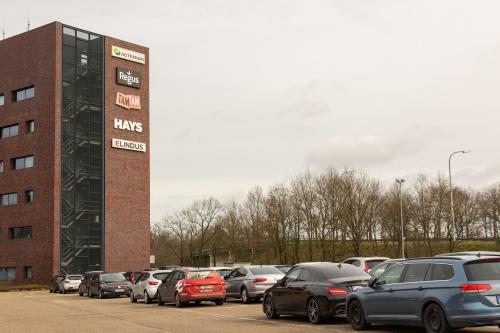 Kantoor te huur op Atealaan 34A, Herentals, zicht op de buitenkant van het gebouw en parkeerplaats vol auto's.