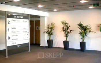 Ingang van een kantoor te huur op Blarenberglaan 2c, Mechelen Noord met strakke bewegwijzering en planten tegen een witte muur.