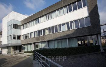 Moderne kantoorgebouw op Blarenberglaan 2c, Mechelen Noord, waar je kantoorruimte kunt huren. Het gebouw heeft een strakke architectuur met grote ramen en een ruime parkeerplaats voor het gemak.