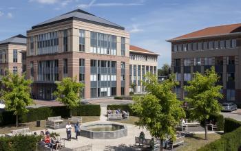 Kantoor te huur gelegen op Schaliënhoevedreef 20E, Mechelen Noord. Buitenzijde van modern kantoorpand met groen park en mensen bezig met een zakelijk gesprek.