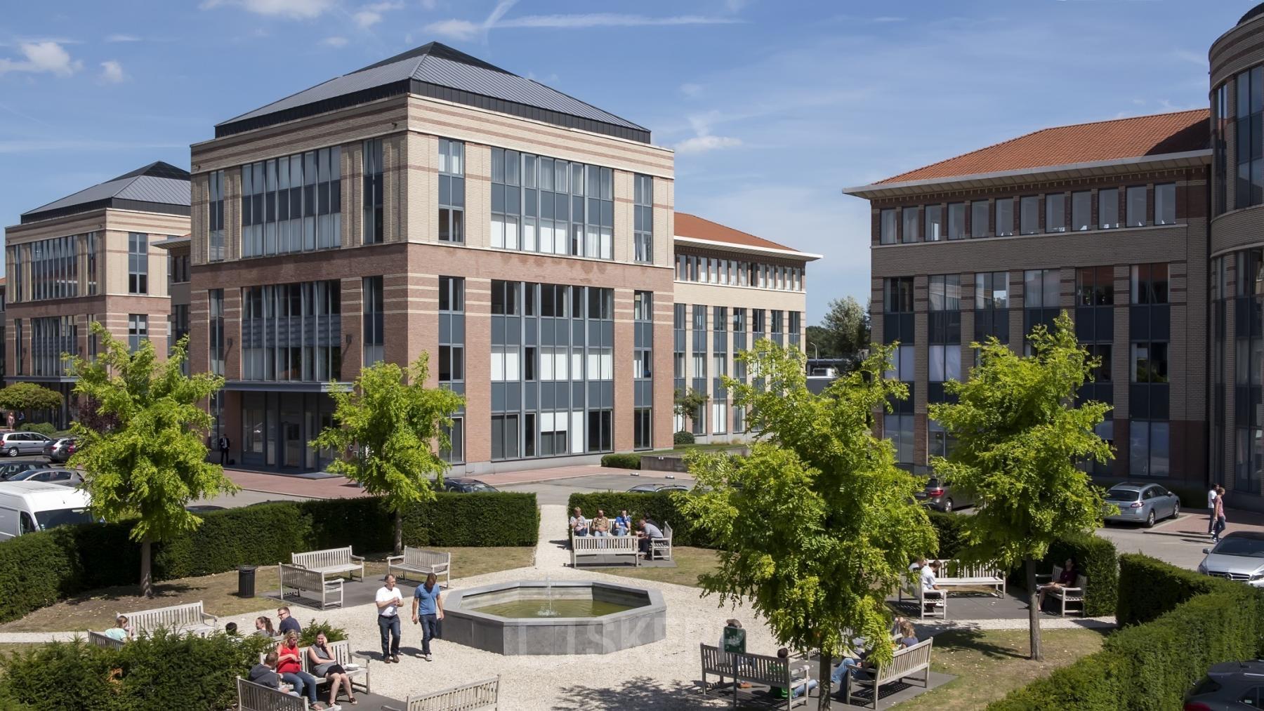 Kantoor te huur gelegen op Schaliënhoevedreef 20E, Mechelen Noord. Buitenzijde van modern kantoorpand met groen park en mensen bezig met een zakelijk gesprek.