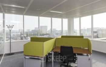 Kantoor te huur in Sint-Agatha-Berchem met grote glazen ramen en uitzicht op stad, voorzien van werkplekken en een frisse inrichting.