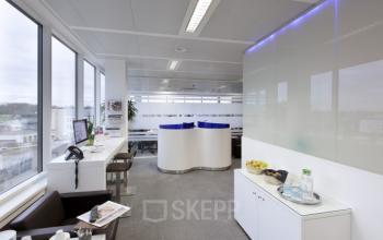 Een moderne kantoorruimte te huur aan de Keizer Karellaan 584 in Sint-Agatha-Berchem, met strakke lijnen en voldoende daglicht. De ruimte is gemeubileerd met zitjes en een werkbank langs het raam.